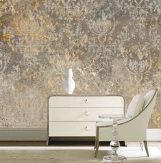 a white dresser and chair in front of a wall with gold leaf designs on it