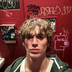 a young man standing in front of a red wall with graffiti on it's walls