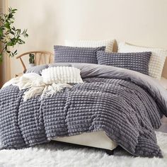 a bed with grey and white comforters in a room next to a plant on the floor