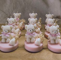 small white teddy bears on pink bases with gold leaves and ribbons around their necks, sitting on a wooden surface