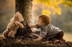 a little boy playing with a teddy bear next to a tree