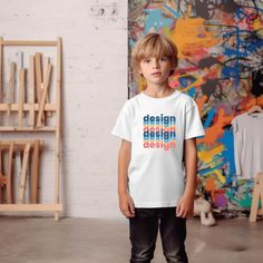 a young boy standing in front of a wall with paintings on it and wearing a t - shirt that says design, design, design