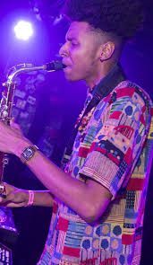 a man that is standing up with a saxophone in his hand and wearing a colorful shirt