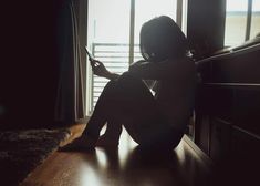 a woman sitting on the floor in front of a window looking at her cell phone