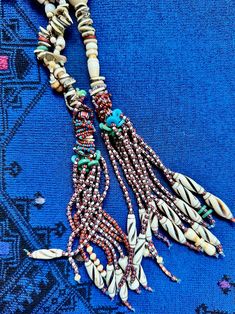 This unique design employs an eclectic array of beads. The beauty is in the details: neutral shades of sand and beach washed shell contrasted with tassels of glass seed beads. The tassels are earthy reds accented by faded aqua and turquoise glass beads. The bead materials include new and old shell and shell beads, bone, glass, and large vintage Lucite beads. The latter are visually pleasing, upcycled and serve a structural purpose without contributing additional weight. Handmade Bohemian Sand-colored Jewelry, Beach Jewelry With Brown Tassels, Bohemian Beige Beads For Beach, Beige Bohemian Beads For Beach, Bohemian Beige Beach Beads, Bohemian Brown Lariat Beaded Necklaces, Bohemian Multi-strand Beach Beads, Bohemian Hand-strung Lariat Beaded Necklace, Hand-strung Bohemian Lariat Beaded Necklaces