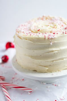 a white frosted cake sitting on top of a plate next to candy canes