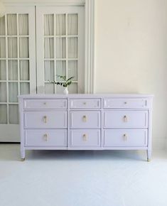 a white dresser sitting in front of a door with glass doors on the side and a vase filled with flowers next to it