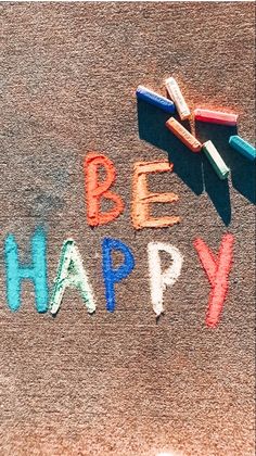 the word be happy written in colored crayons on top of a brown carpet