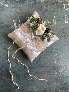 a small pillow with flowers and pine cones on it is tied to a string, sitting on the ground