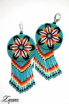 two pairs of beaded earrings with fringes and beads hanging from hooks on a white background