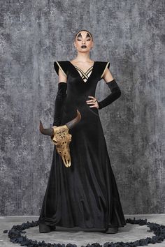 a woman in a black dress with horns on her head is standing next to a cow skull