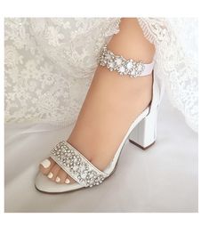 Our white wedding shoe, promises to cause waves amongst your wedding guests. Crafted in soft white leather and adorned with iridescent, light-catching rhinestones.  The luxurious leather lining is cushioned in all the right places to ensure ultimate comfort. Whilst the delicate straps and sturdy leather-wrapped block heel keep you feeling secure. You can wear them either with the leather ankle strap (Included)  or with the satin embroidered ribbon All of the embellishments are handsewn onto the Open Toe Heels With 4-inch Heel For Bridal Shower, Wedding Sandals With 4-inch Heel And Round Toe, Wedding Shoes With 4-inch Open Heel, Embellished Wedding Shoes For Prom With Block Heel, Embellished Block Heel Wedding Shoes For Prom, Elegant Block Heel Sandals For Bridal Shower, Open Toe Wedding Shoes With Rhinestones, Elegant Open Toe Block Heels For Bridal Shower, Wedding Heels With Padded Block Heel