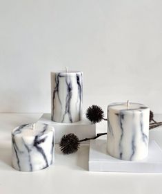 three marbled candles sitting on top of a white table next to dried thistle flowers