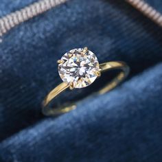 an engagement ring sits on top of a blue velvet box with a diamond in it