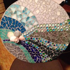 a mosaic plate with shells and sea glass on it sitting on a table next to a keyboard