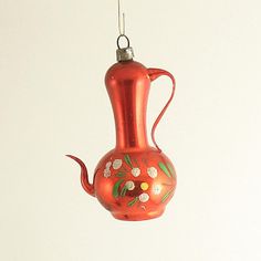 a red glass vase with flowers on it hanging from a hook ornament in the shape of a teapot