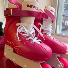 two pink roller skates sitting on top of a red table next to a window