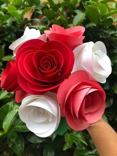 red and white paper flowers are held by someone's hand in front of green leaves