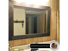 a bathroom mirror sitting on top of a wooden wall next to a white sink under a faucet