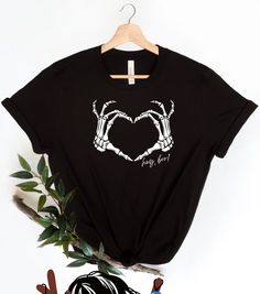 Beautiful skull with heart t-shirt for any occasion. *ABOUT OUR SHIRT*¨ -100% Airlume combed and ringspun cotton (fiber content may vary for different colors) -Light fabric (4.2 oz/yd² (142 g/m²) -Runs true to size ¨*WASH/CARE INSTRUCTIONS*¨ -Wash before use. -Inside out, wash with delicate cycle. -Wash with cold water. -Do not bleach. -Do not iron directly onto the design. -Do not dry clean. ¨*HOW TO ORDER*¨ -Before you place the order, please review all the information. -Select the garment SIZE and garment COLOR. -Select the quantify. -Click Add to Cart. -For multiple items go back to the listing and repeat the steps. Thank you for trusting us!. Black Top With Heart Graphic As Gift, Trendy Black T-shirt For Gift, Unisex Black T-shirt For Gift, Casual Halloween T-shirt For Gift, Black T-shirt With Heart Graphic As Gift, Black T-shirt With Skull Print For Fans, Alternative White T-shirt With Skull Print, Gothic T-shirt With Skull Print For Alternative Fashion, Cotton T-shirt With Custom Skull Print