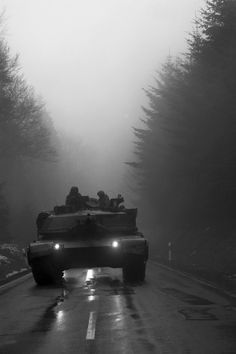 an armored vehicle driving down a road in the rain with headlights shining on it's side