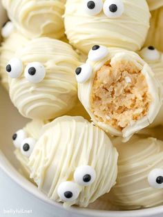 some white chocolate balls with googly eyes on them are in a bowl and have been cut open to show the inside