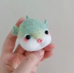 a hand holding a tiny green and white stuffed animal