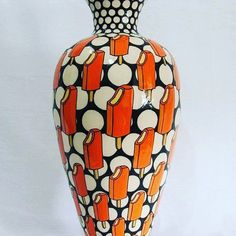 an orange and black vase with polka dot designs on it's sides, sitting against a white background