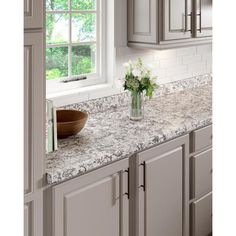 a kitchen counter top with a bowl and flowers on it in front of a window