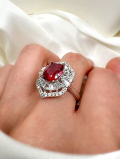 a close up of a person's hand holding a ring with a red stone