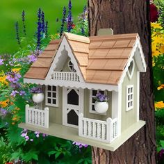 a bird house hanging from the side of a tree in front of flowers and trees