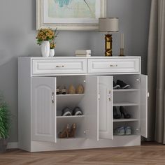 a white cabinet with open doors and shoes on it in front of a large painting