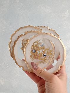 a person holding three plates with gold and white designs on them, one has eyes in the middle