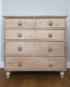 an old wooden dresser with knobs on the top and bottom drawers, in front of a white wall