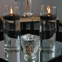 two clear glass vases with lit candles in them sitting on a mirrored table top