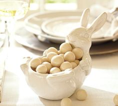 a bowl filled with white chocolate eggs sitting on top of a table next to plates