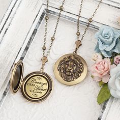 two necklaces with lions on them sitting next to flowers and an old window frame