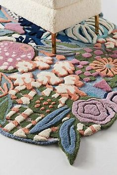 an area rug with flowers on it and a chair next to it in front of a white wall