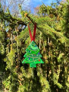 a green christmas tree ornament hanging from a pine tree in front of blue sky