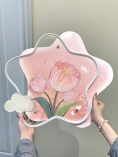 a woman is holding up a pink flower shaped mirror with flowers painted on it and clouds in the background