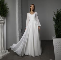 a woman in a white wedding dress standing next to a potted plant on the floor