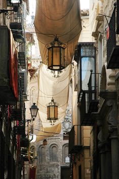 an alleyway with several lamps and lanterns hanging from the ceiling in front of buildings