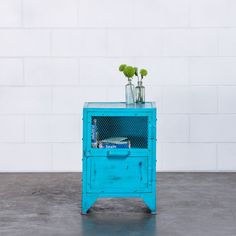 a blue cabinet with two vases and flowers on top, against a white brick wall