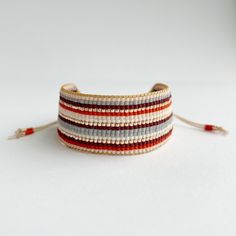 a close up of a bracelet on a white surface with red, grey and white beads