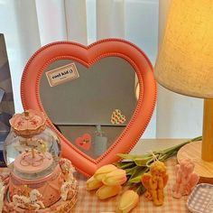 a heart shaped mirror sitting on top of a table next to flowers and other items