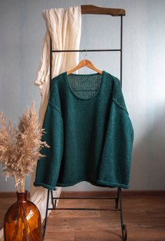 a green sweater sitting on top of a chair next to a vase with dried grass