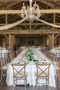 a long table with white linens and greenery in front of a chandelier