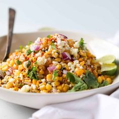 a white bowl filled with corn salad and garnished with cilantro, lime wedges