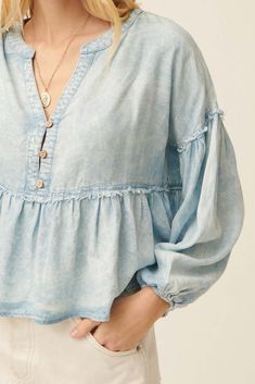 Acid washed denim blouse. Split neckline. 3-button closure with wood buttons. Long bubble sleeves with elastic cuffs. Drop shoulder. Exposed seams with frayed, raw-edge detailing. Flared ruffle hem. Babydoll silhouette. Loose fit. 100% Cotton. Imported. Designed in LA. Model wears size S. Exposed Seams, Wood Buttons, Acid Wash Denim, Denim Blouse, Babydoll Top, Washed Denim, Acid Wash, Denim Blue, Raw Edge