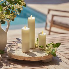 four lit candles sitting on a table next to a potted plant